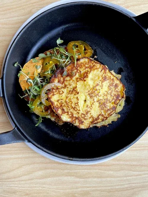 Cast-iron skillet with stacked pancakes, microgreens, sliced jalapeños, and red sauce.