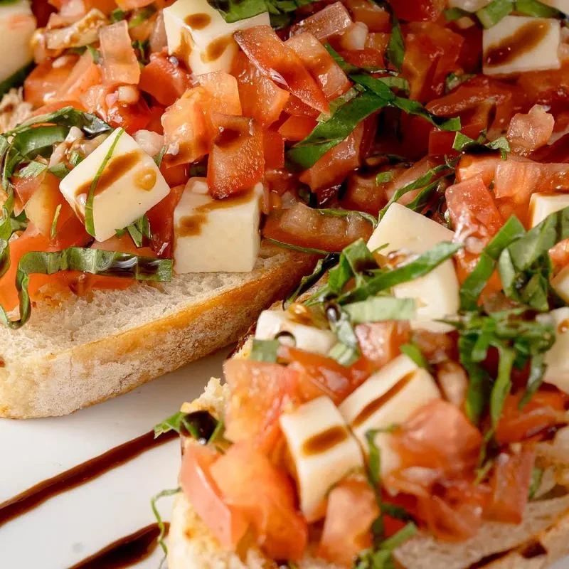 Two bruschetta topped with tomatoes, mozzarella, basil, drizzled with balsamic glaze.