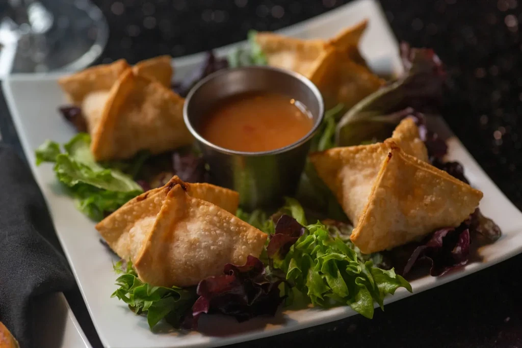 Plate of five crispy, golden-brown fried wontons with dipping sauce.