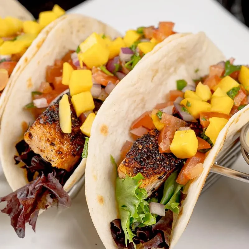 Three fish tacos with blackened fish, mango salsa, and fresh greens.