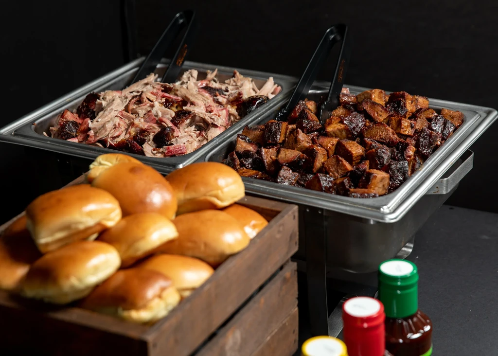 Buffet setup with pulled pork, brisket burnt ends, rolls, and sauces.