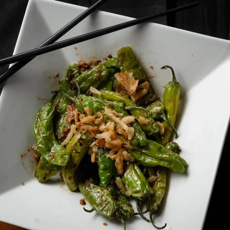 Overhead: Sautéed green peppers, crispy shallots, white bowl, and chopsticks.