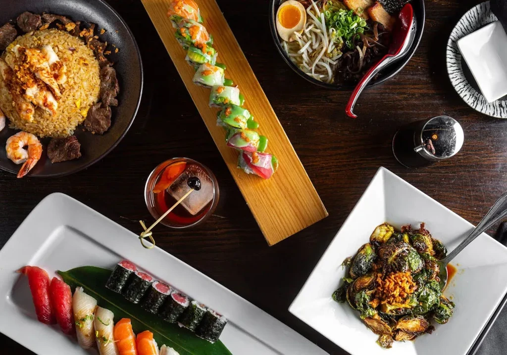 Overhead photo of sushi, ramen, fried rice, brussels sprouts, and cocktail.