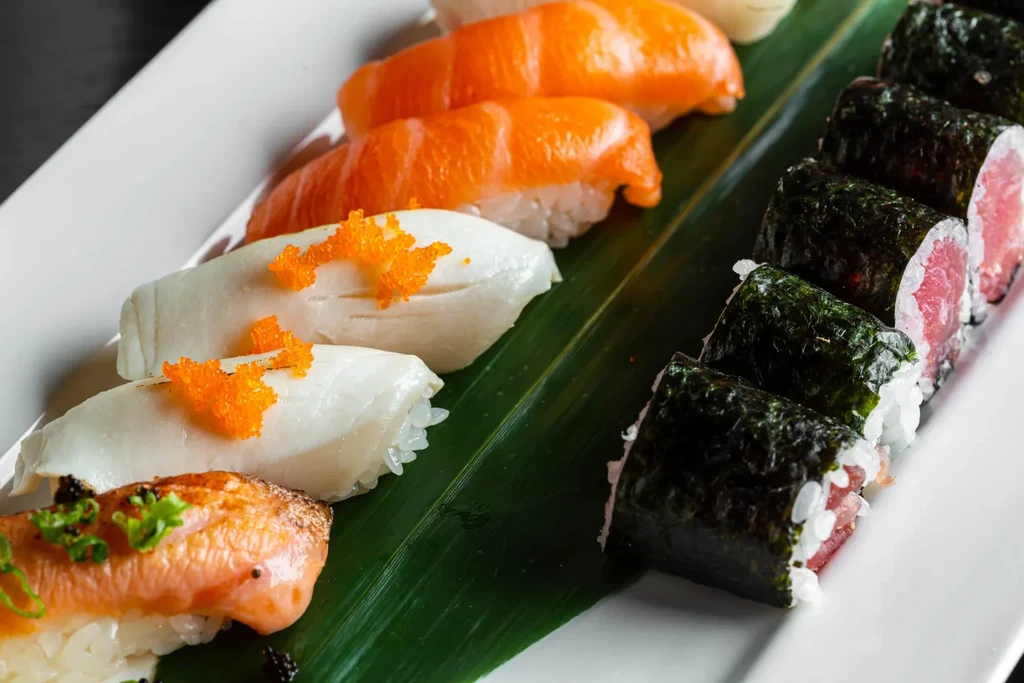 Close-up of nigiri and maki sushi separated by a green leaf.
