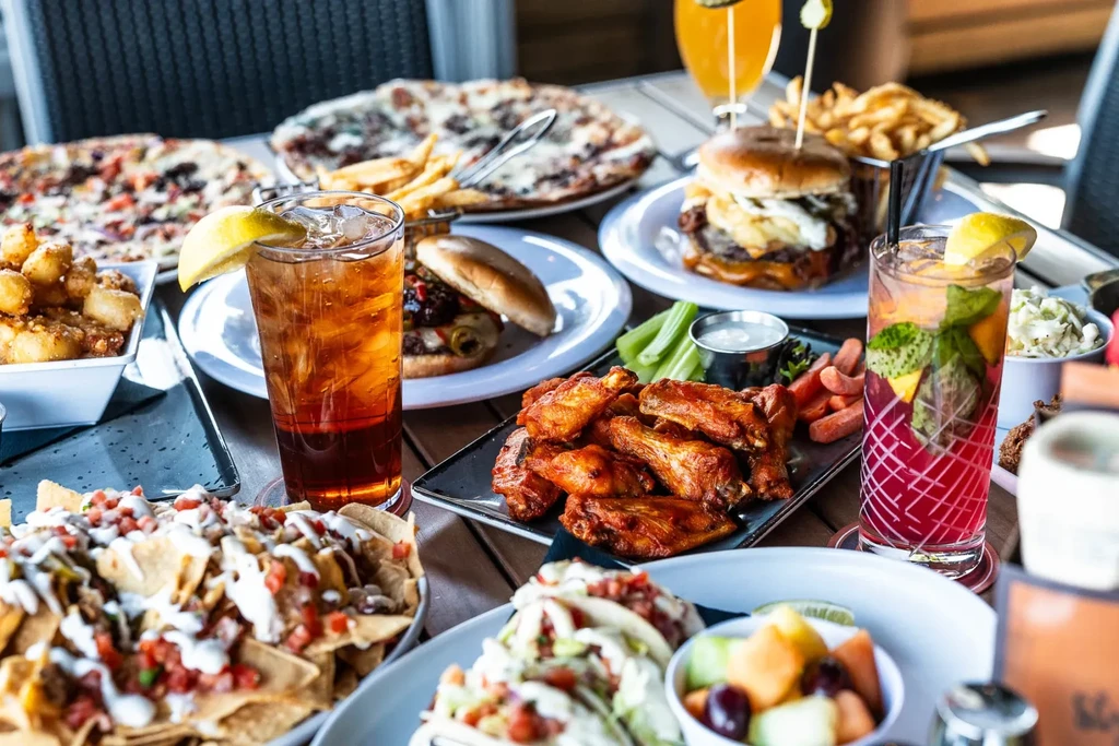 Table laden with nachos, tacos, wings, burgers, pizzas, and drinks.