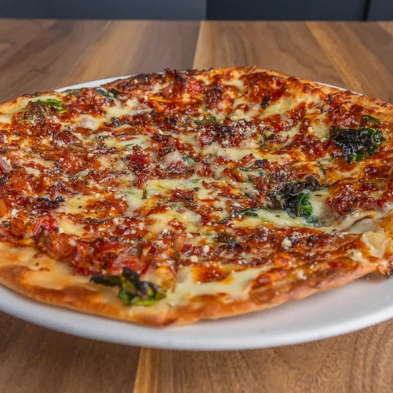 Sliced pizza with melted cheese, crumbled toppings, green herbs, charred crust.