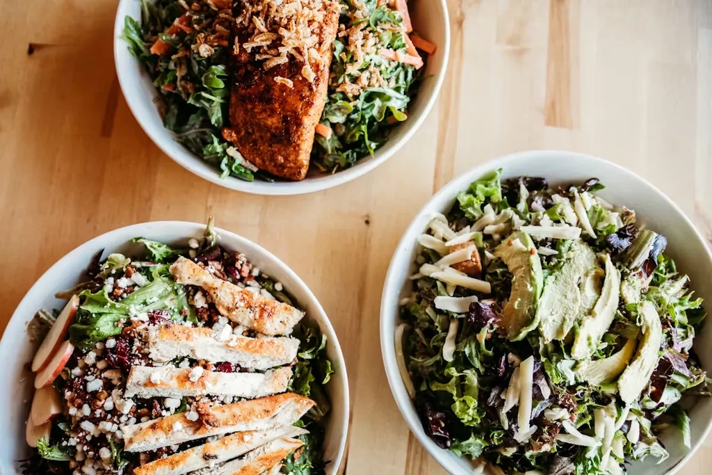 Three distinct, colorful salad bowls with fish, chicken, avocado.