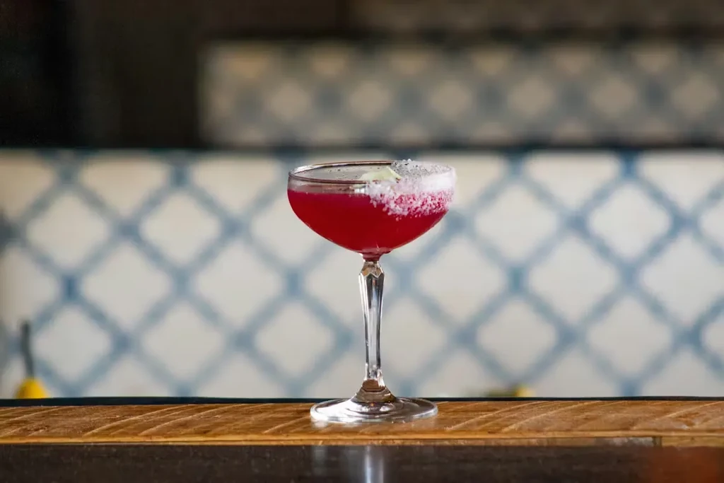 Vibrant magenta cocktail in a coupe glass with a sugared rim.