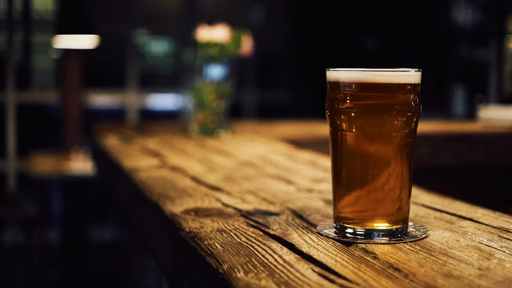 Golden amber beer in a glass on a rustic wooden bar.