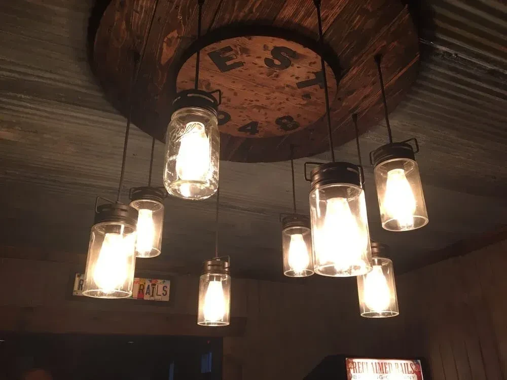 Rustic wooden spool chandelier, mason jar lights, with "EST 1948" text.