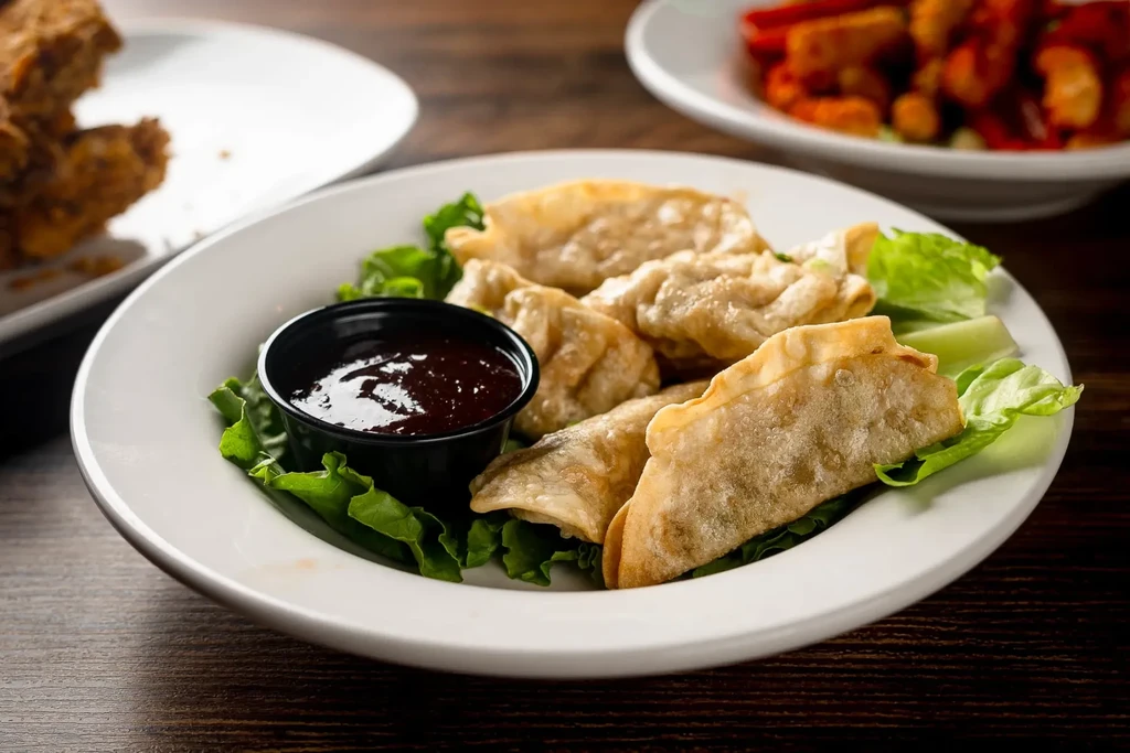 Crispy golden-brown fried dumplings on lettuce with dipping sauce.