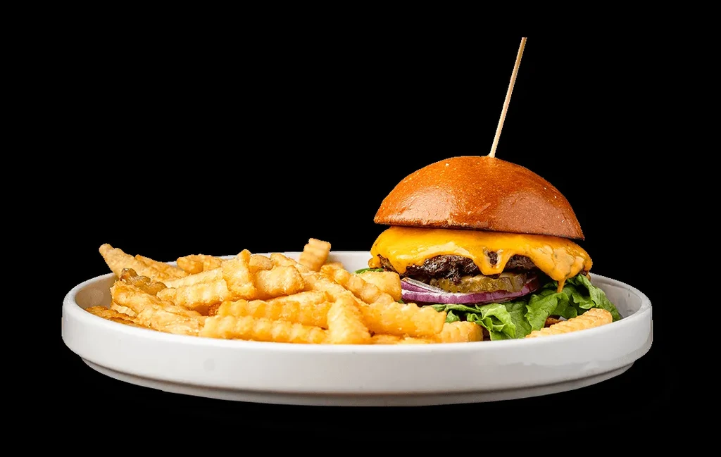 Studio shot: Cheeseburger, crinkle-cut fries on white plate, black background.