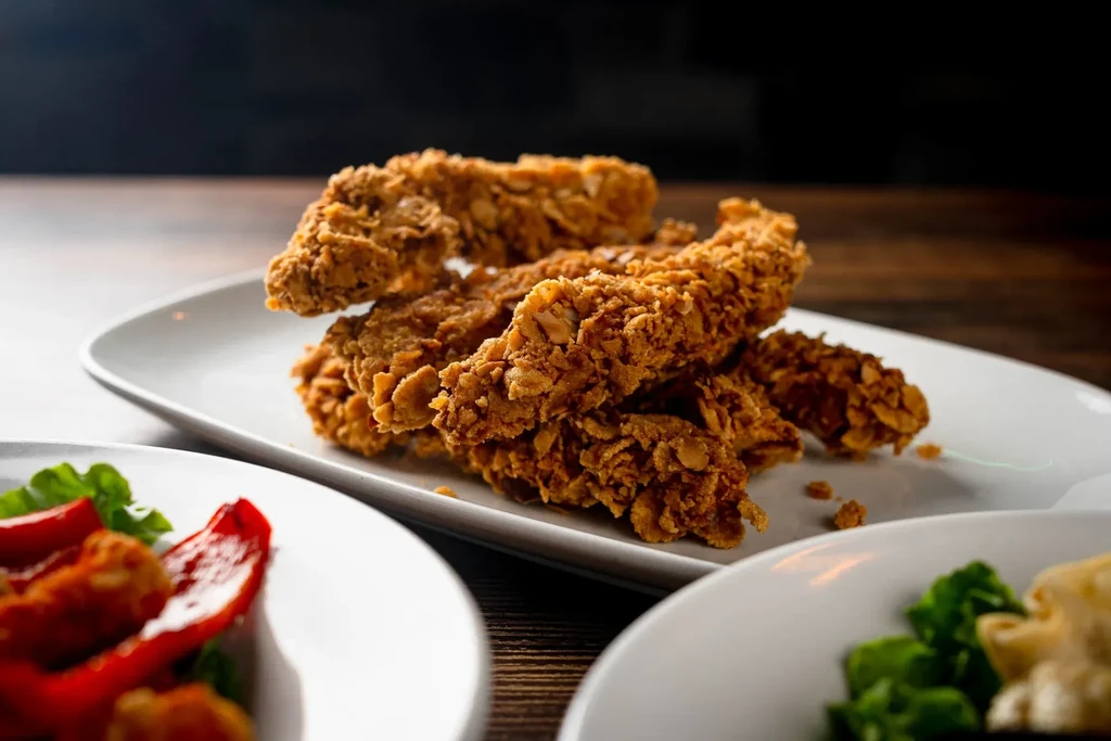 Crispy golden-brown fried chicken tenders piled on a white plate with sides.