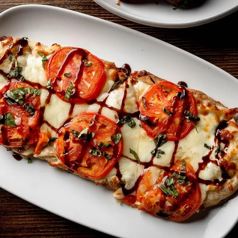 Rectangular flatbread with cheese, tomatoes, basil, and balsamic glaze.