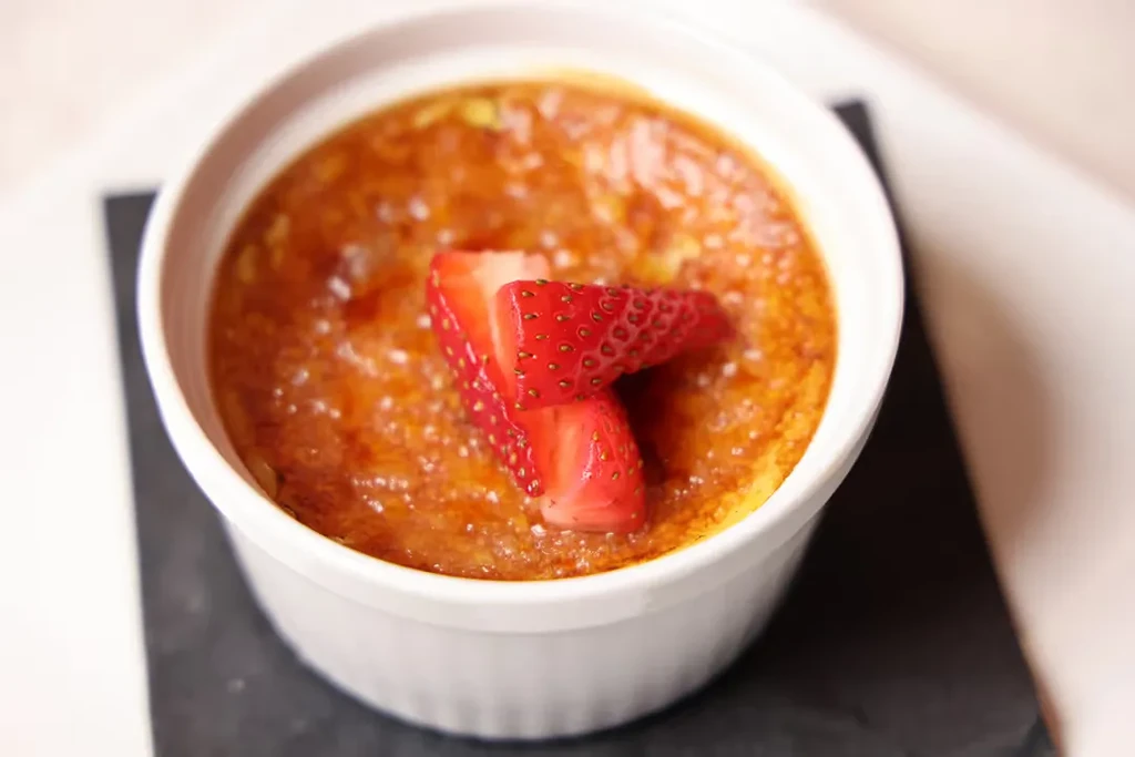 Crème brûlée with golden crispy topping and fresh strawberry halves.
