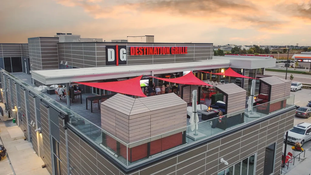 Aerial view: Destination Grille's rooftop patio with red sails and people.