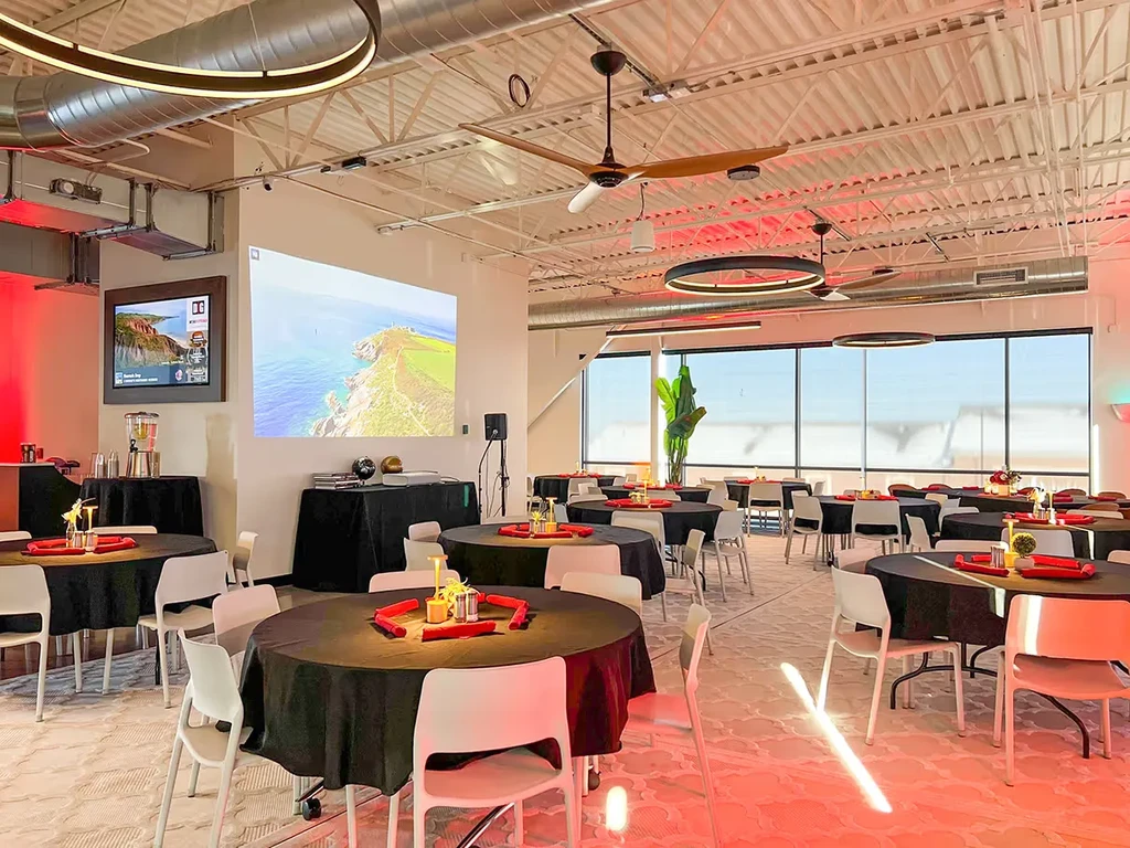 Modern event hall with black tables, red lighting, and projector screens.