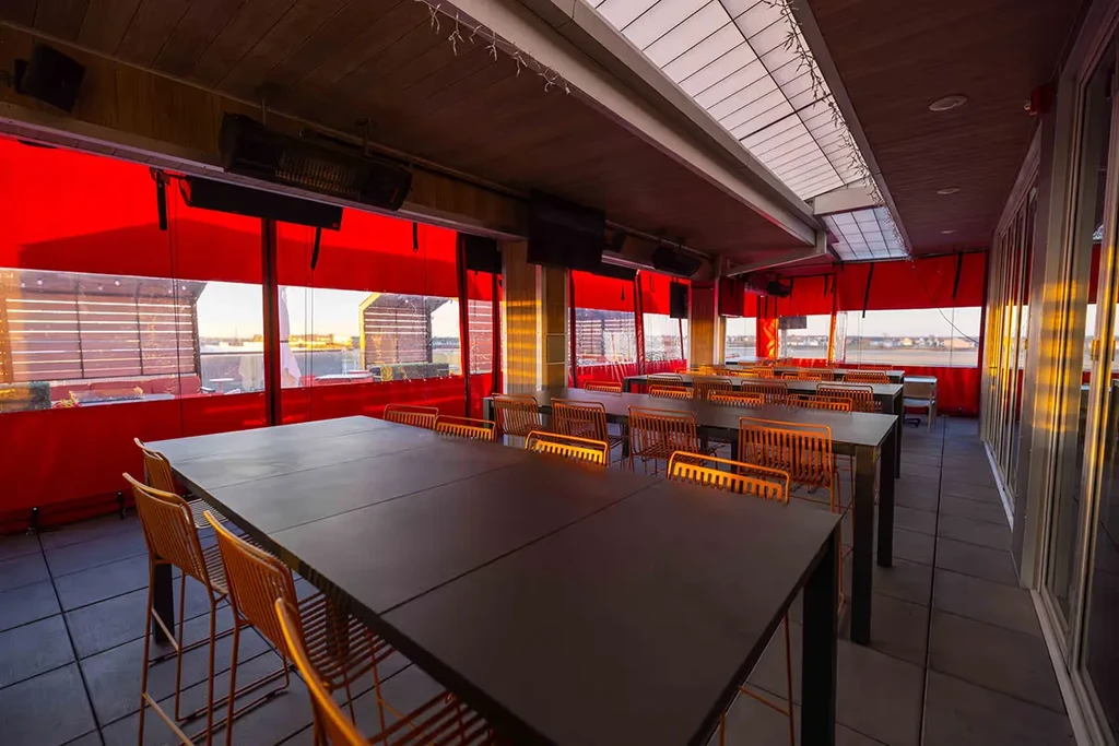 Sunlit modern restaurant dining room with orange chairs and dark tables.