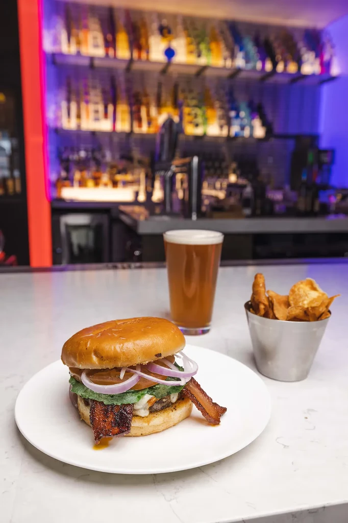 Gourmet burger, amber beer, and chips on a bar counter.