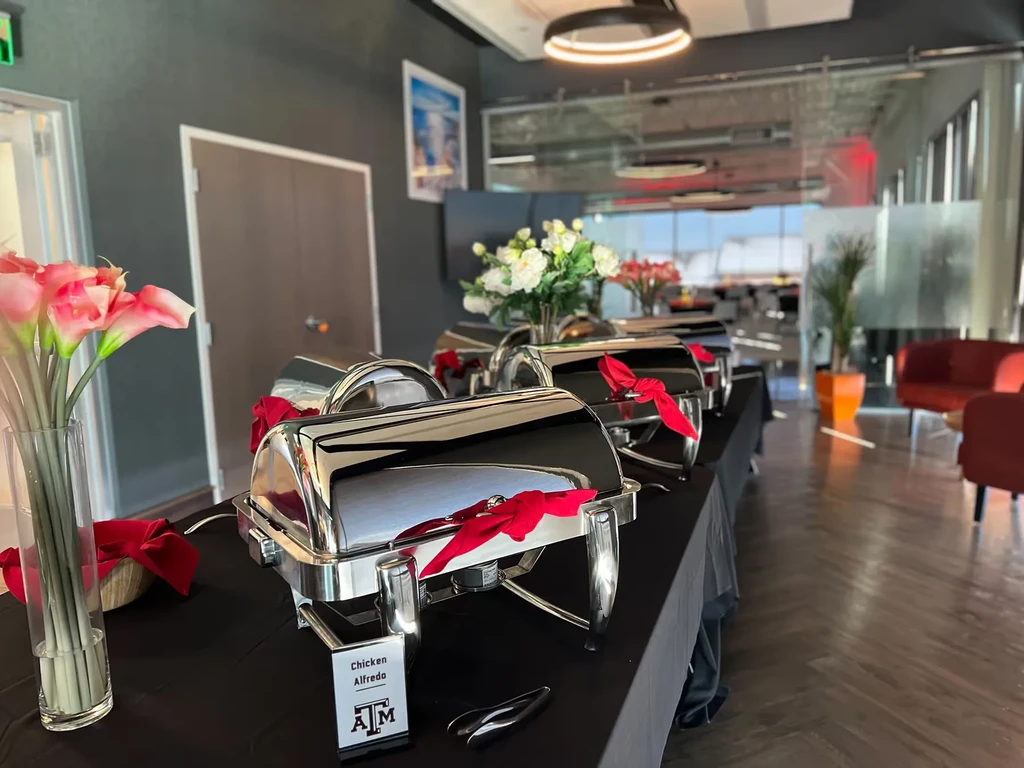 Modern buffet with chafing dishes, pink lilies, and A&M Chicken Alfredo sign.