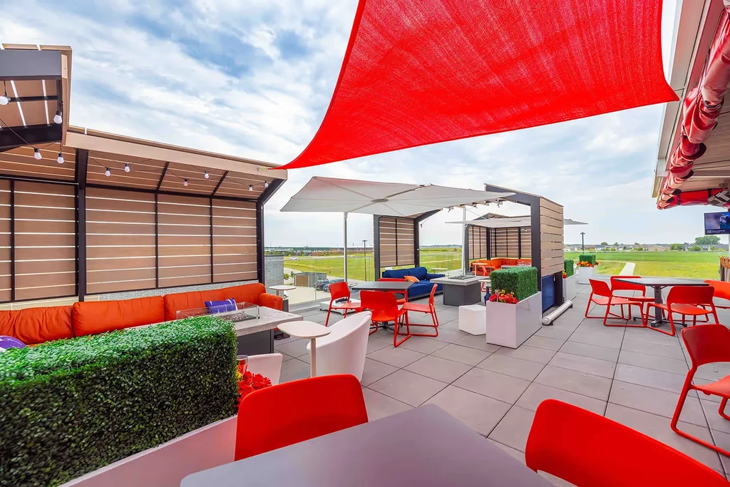 Modern outdoor patio with colorful seating, fire pits, pergolas, and green view.