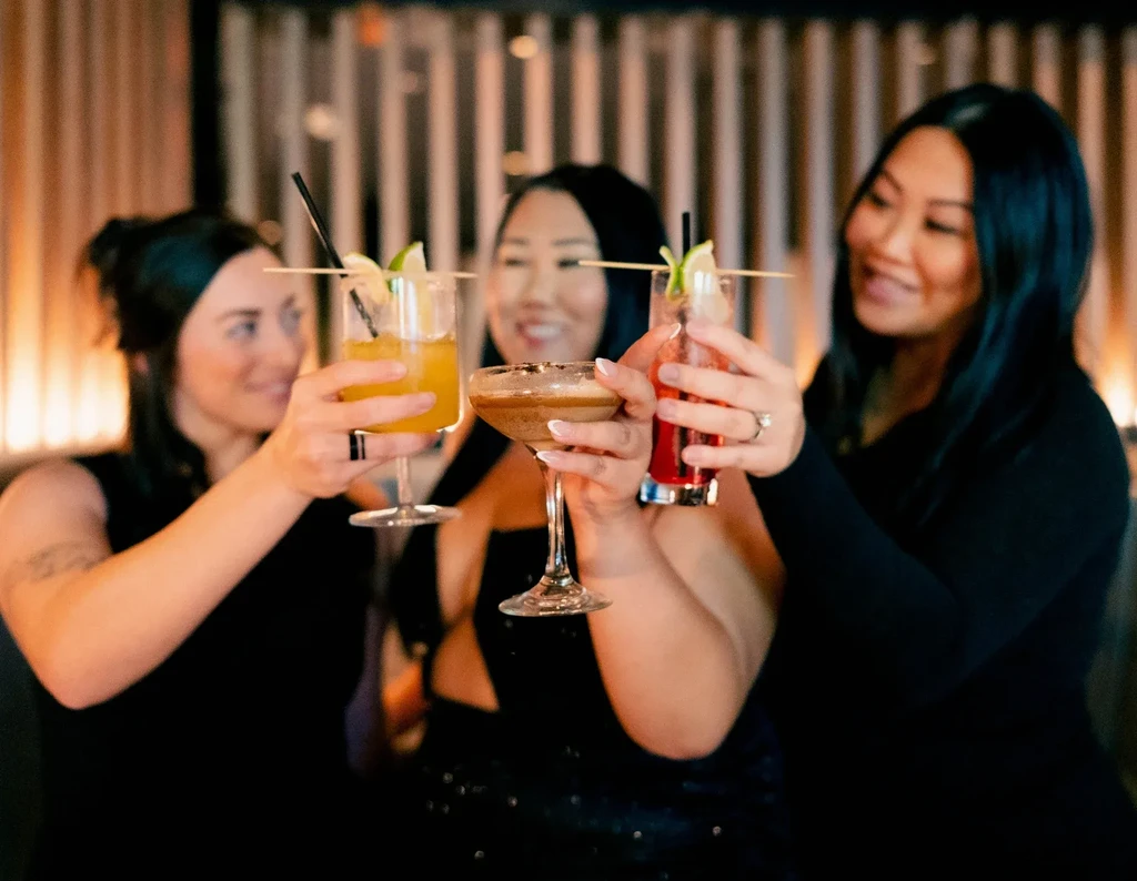 Three women toasting various cocktails, including an espresso martini.