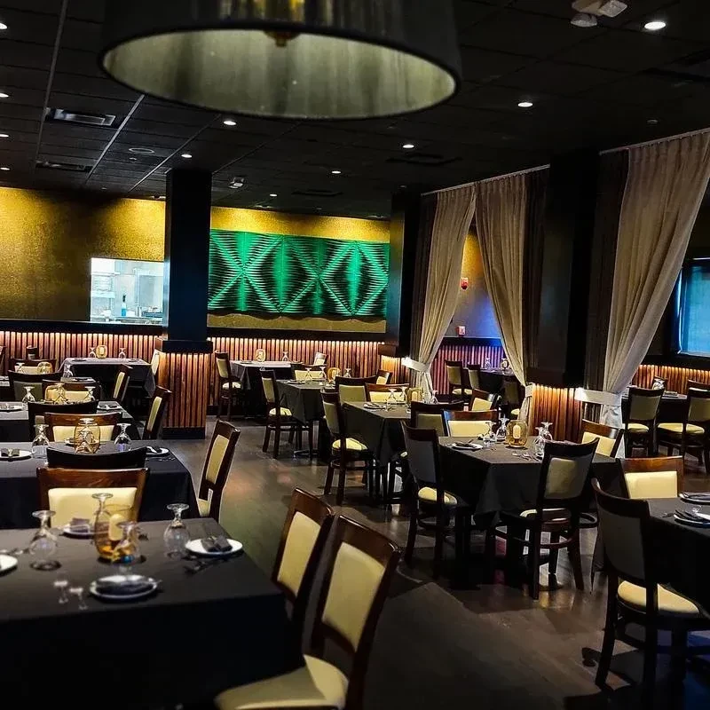 Empty, modern upscale restaurant interior, dark tables, warm lighting, geometric wall.
