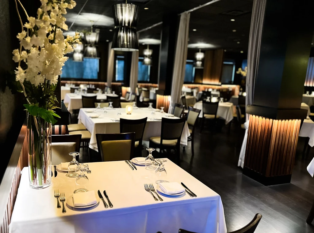 Upscale restaurant interior with elegantly set tables and white floral bouquets.
