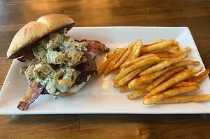 Open burger with bacon, onion rings, sauce, and seasoned fries on plate.