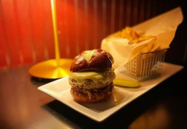 Pretzel bun burger with melted cheese, golden fries, and pickle.