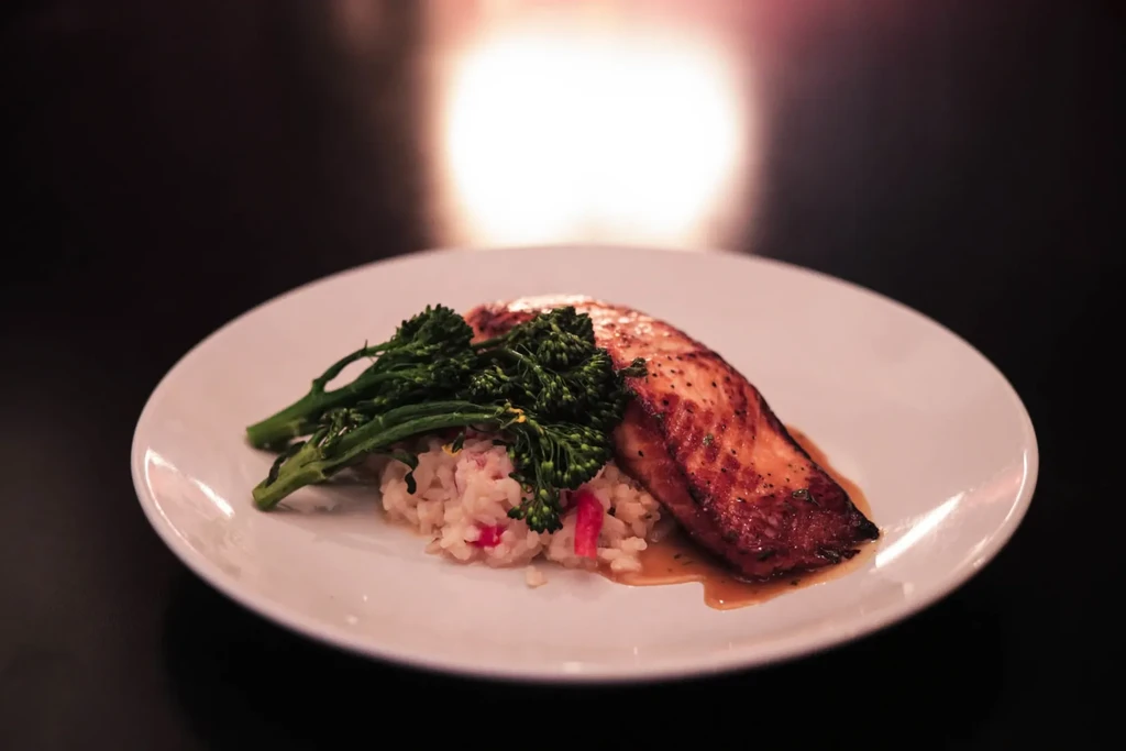 Crispy seared salmon, creamy risotto, and broccolini on white plate.