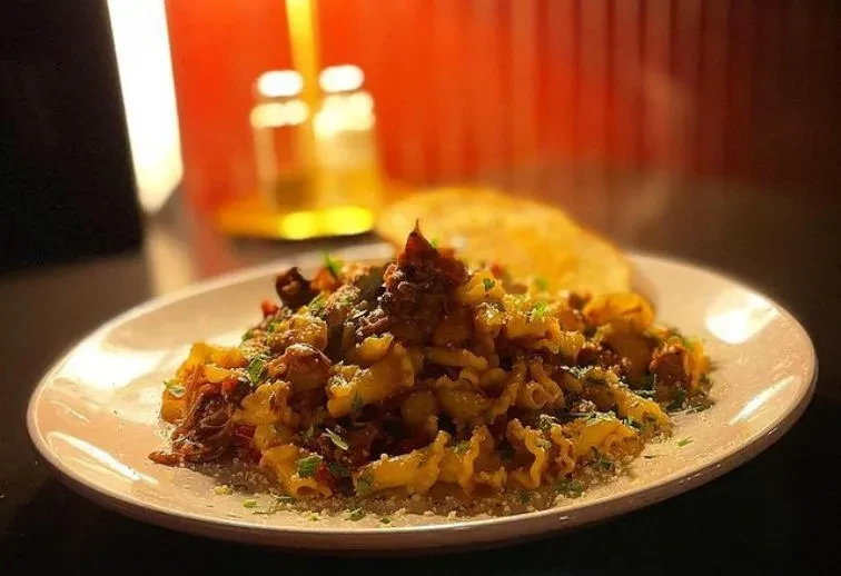 Conchiglie pasta with dark sauce, grated cheese, and green herbs.