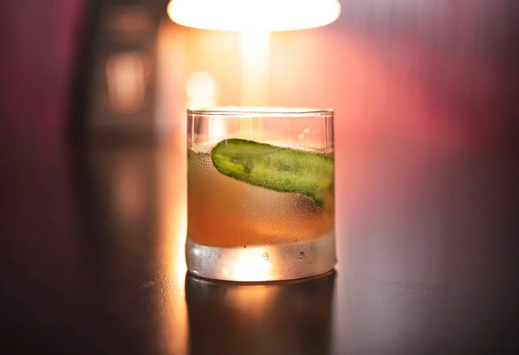 Amber drink in a rocks glass with cucumber and ice.