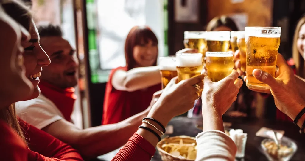 Smiling people clinking glasses of amber beer in a lively toast.