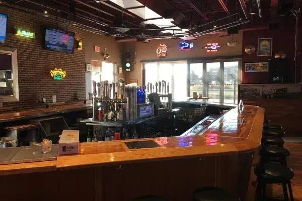 Empty casual bar interior with L-shaped counter, taps, TVs, neon signs.
