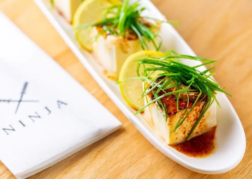 Seared tofu with scallions, lemon, and a reddish-brown sauce.