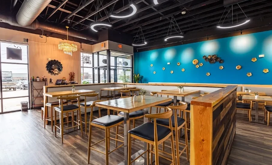 Modern industrial restaurant interior featuring high-top tables and a turquoise decorative wall.