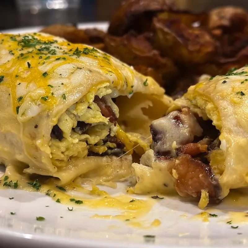 Breakfast burrito halves with eggs, melted cheese, bacon, and herbs.