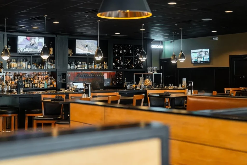 Modern bar area with stocked bottles, TVs, and adjacent dining space.