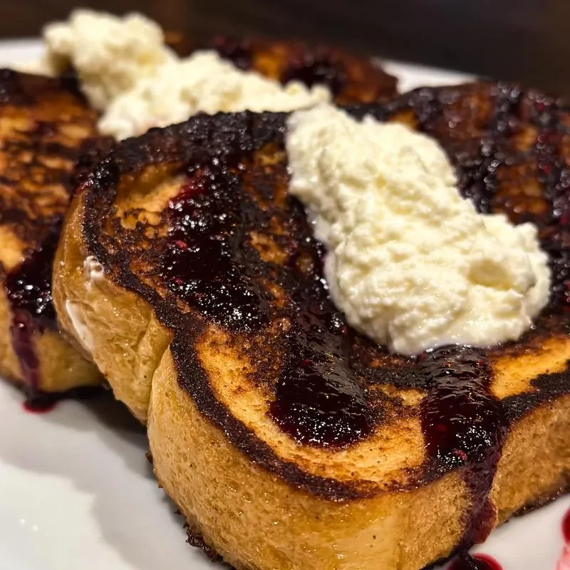 Golden French toast slices topped with dark berry compote and cream.