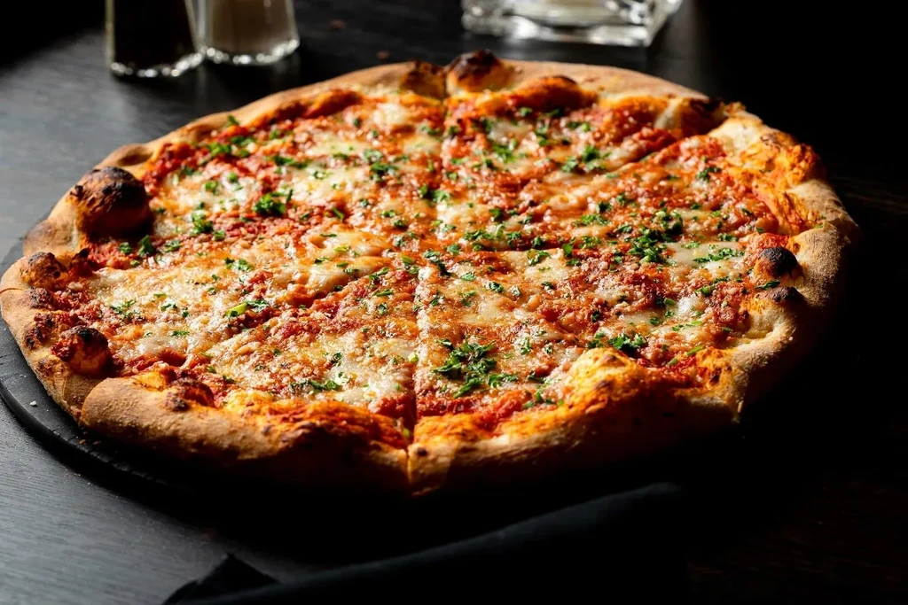 Warm, sliced pizza with golden crust, melted cheese, and fresh herbs.