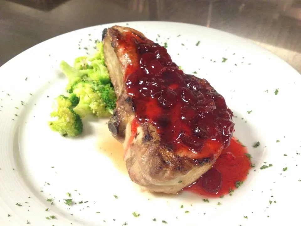 Close-up of a pork chop with red fruit sauce and steamed broccoli.