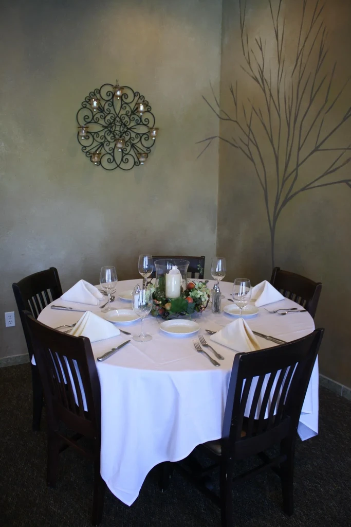 Round restaurant dining table set with white dishes, candle, and wall decor.