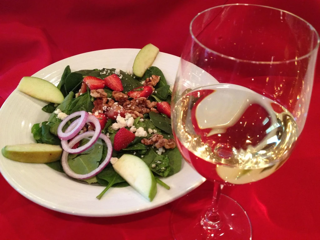Spinach salad with strawberries, feta, walnuts, and white wine on red cloth.