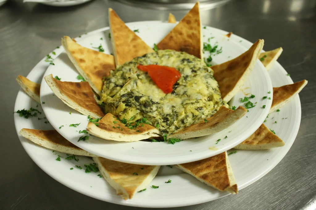 Creamy green dip with red garnish, surrounded by toasted pita.