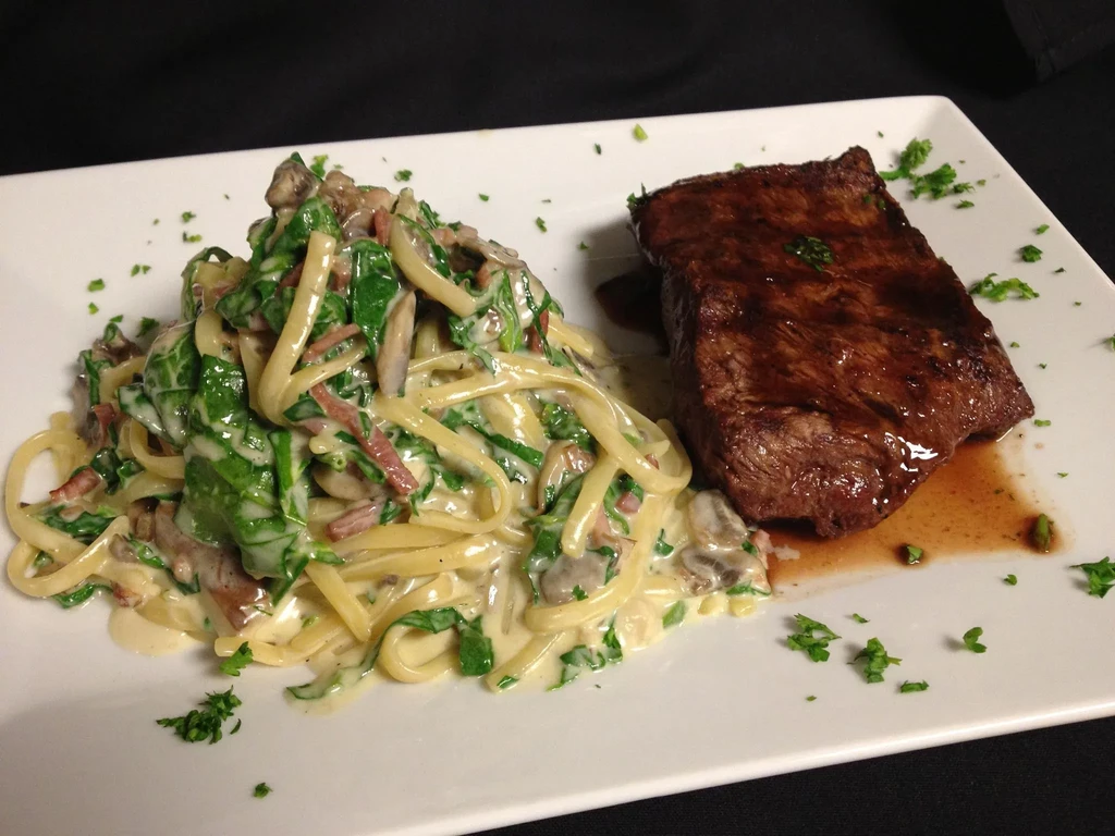 Meticulously plated seared steak and creamy pasta on white.