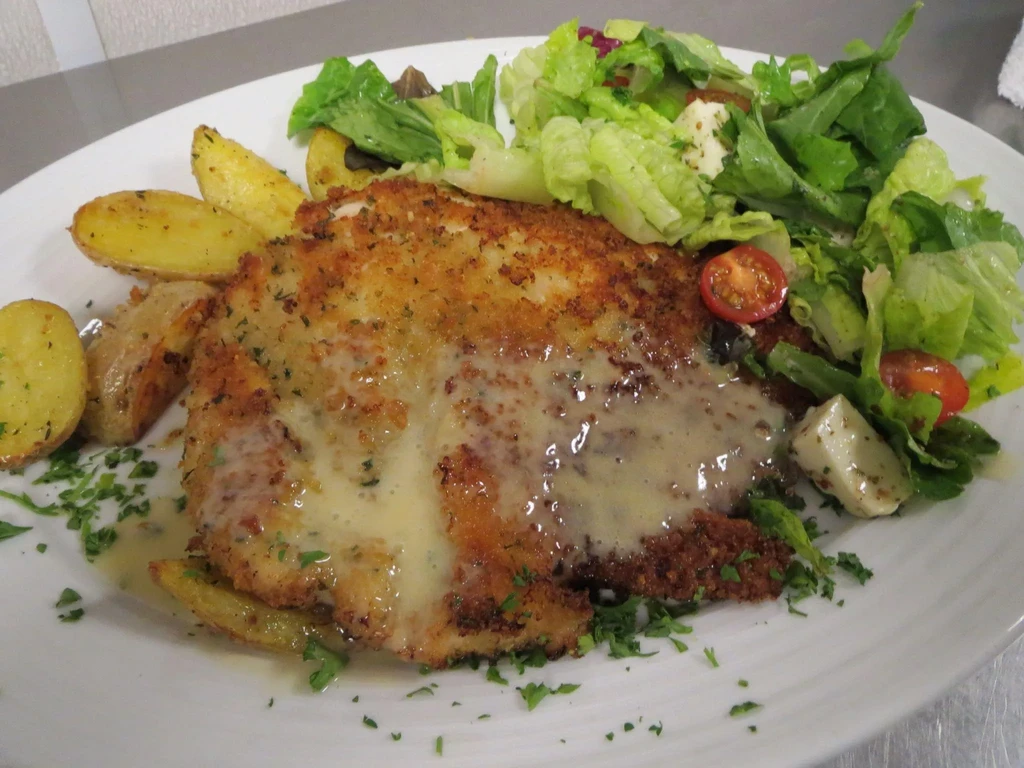 Golden-brown cutlet, creamy sauce, roasted potatoes, and a side salad.