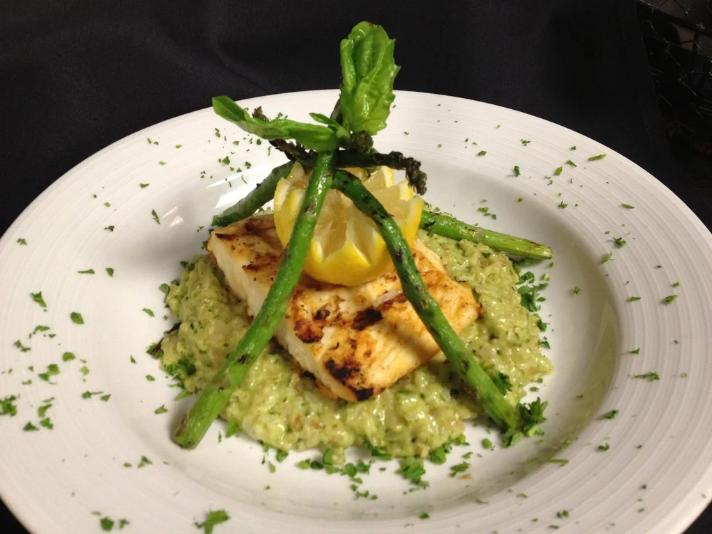 Artistically plated grilled fish, risotto, asparagus, lemon, and parsley.