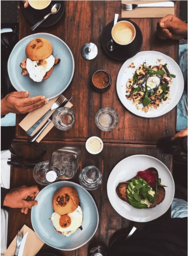 Overhead photo of shared brunch with four plates, coffee, and hands.