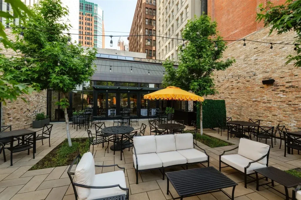 Inviting urban patio with mixed seating, green trees, and yellow umbrella.